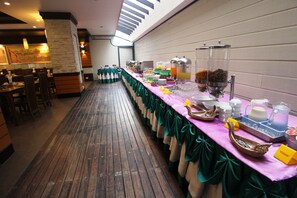 A buffet setup with a long table covered in a green tablecloth, various food items, and drink dispensers.