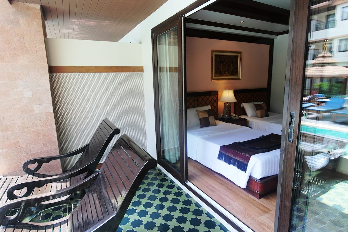 A hotel room with a bed, a nightstand, a lamp, and a view of a pool through a glass door.