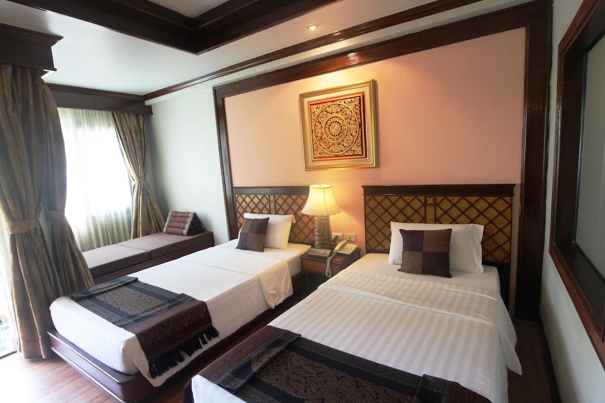 A hotel room with two single beds, a nightstand with a lamp, a decorative wall hanging, and a window with curtains.