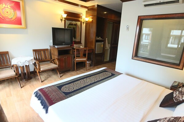 A hotel room with a bed, a desk with a television, a chair, a small table with a lace tablecloth, and a large window. - P.P. Palmtree Resort (Ko Phi Phi)