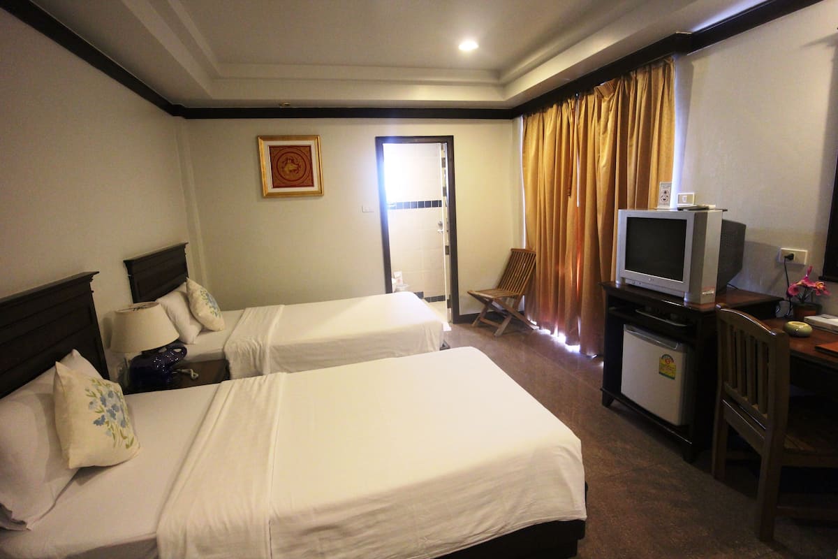 A hotel room with two beds, a television, a small refrigerator, and a desk with a chair.