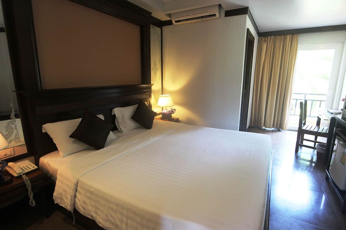 A hotel room with a large bed, a bedside telephone, a lamp, and a view of the outside balcony.