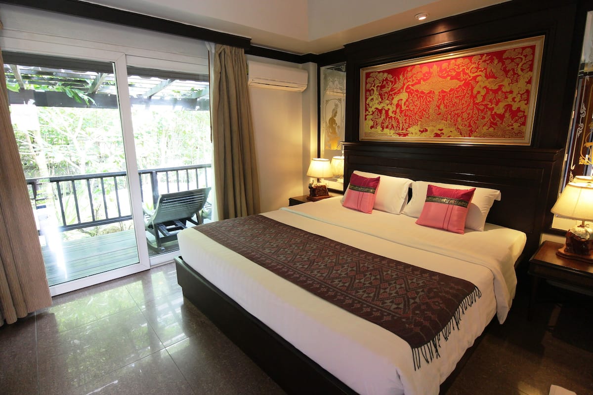 A hotel room with a large bed, a balcony with a chair, and a large decorative wall piece.
