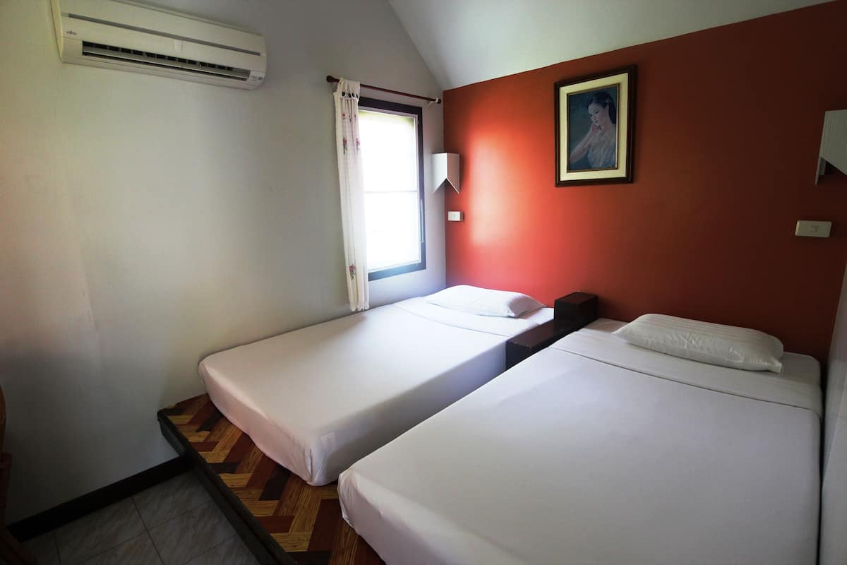 A room with two single beds, a window with a curtain, an air conditioner, and a framed picture on the wall.