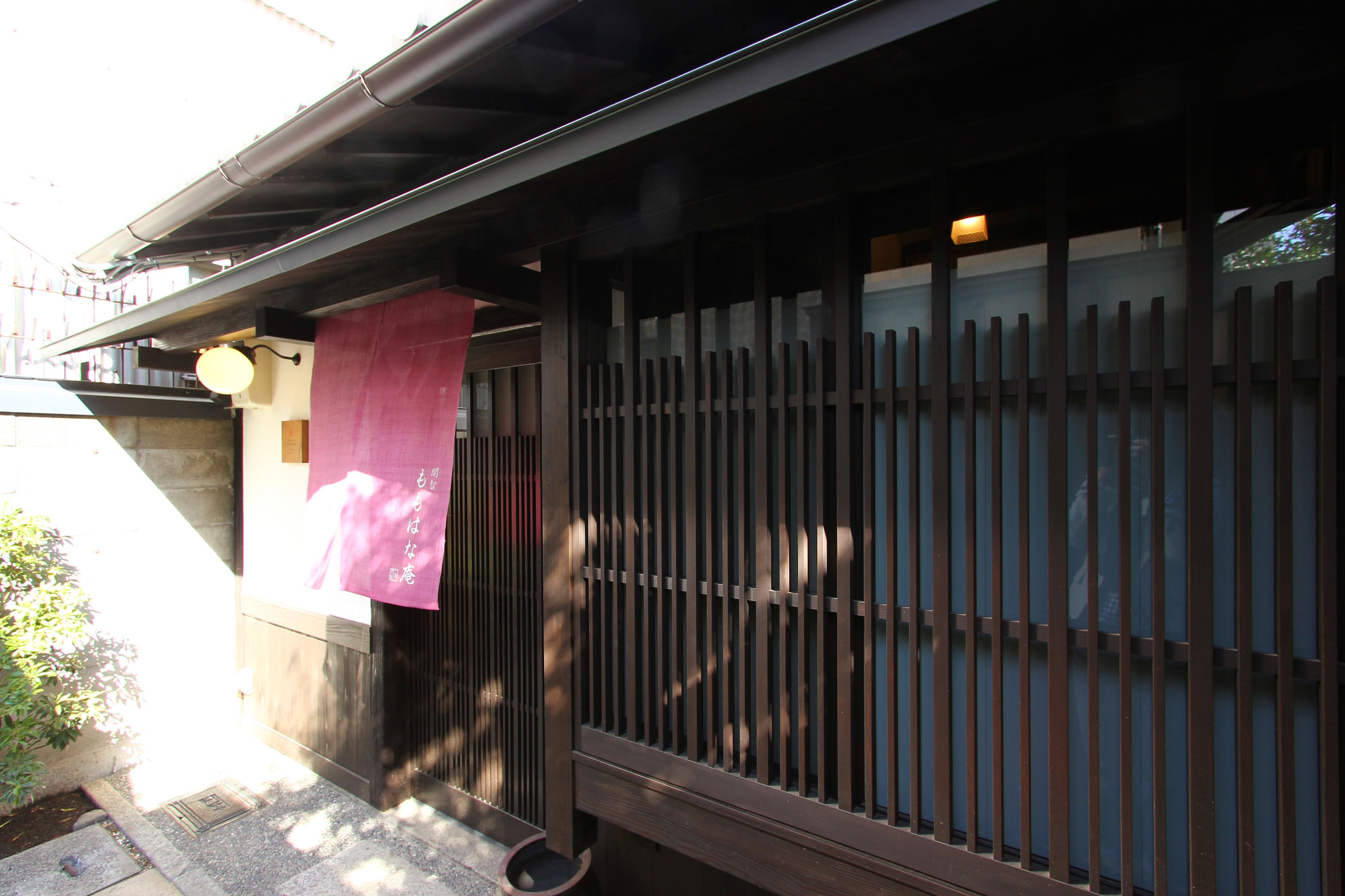 A traditional Japanese building with a wooden exterior, a sliding door with vertical slats, and a small awning.