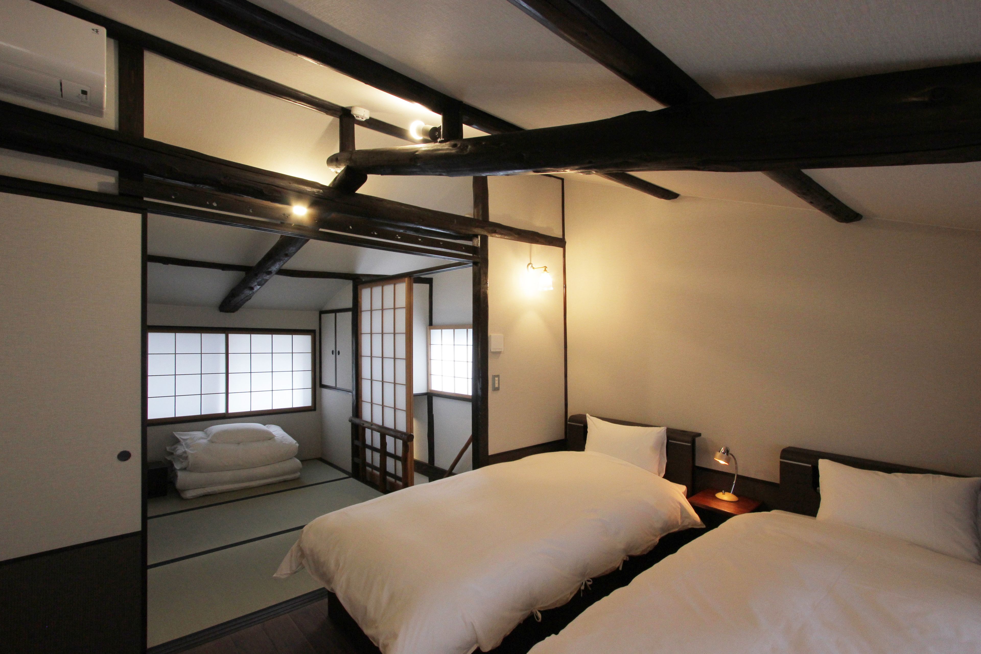 A traditional Japanese-style bedroom with tatami flooring, a sliding door, and a low ceiling with exposed beams.