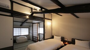 Un dormitorio de estilo japonés tradicional con suelo de tatami, puertas correderas y techo bajo con vigas a la vista.