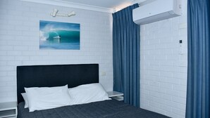 Ein Hotelzimmer mit Bett, einer weißen Ziegelwand, einem Gemälde eines Surfers und einer Klimaanlage.