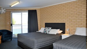 Ein Hotelzimmer mit Backsteinwand, einem großen Bett mit grauer Bettwäsche, einem Nachttisch mit Lampe, einem Stuhl und einer Schiebetür zu einem Balkon.