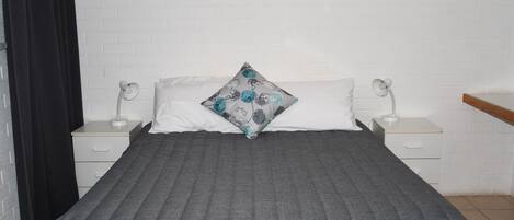 A bed with a grey quilt, two bedside tables with lamps, a white brick wall, and a black curtain.