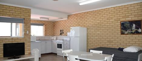 Een compacte kamer met een kitchenette, een eethoek en een bed.