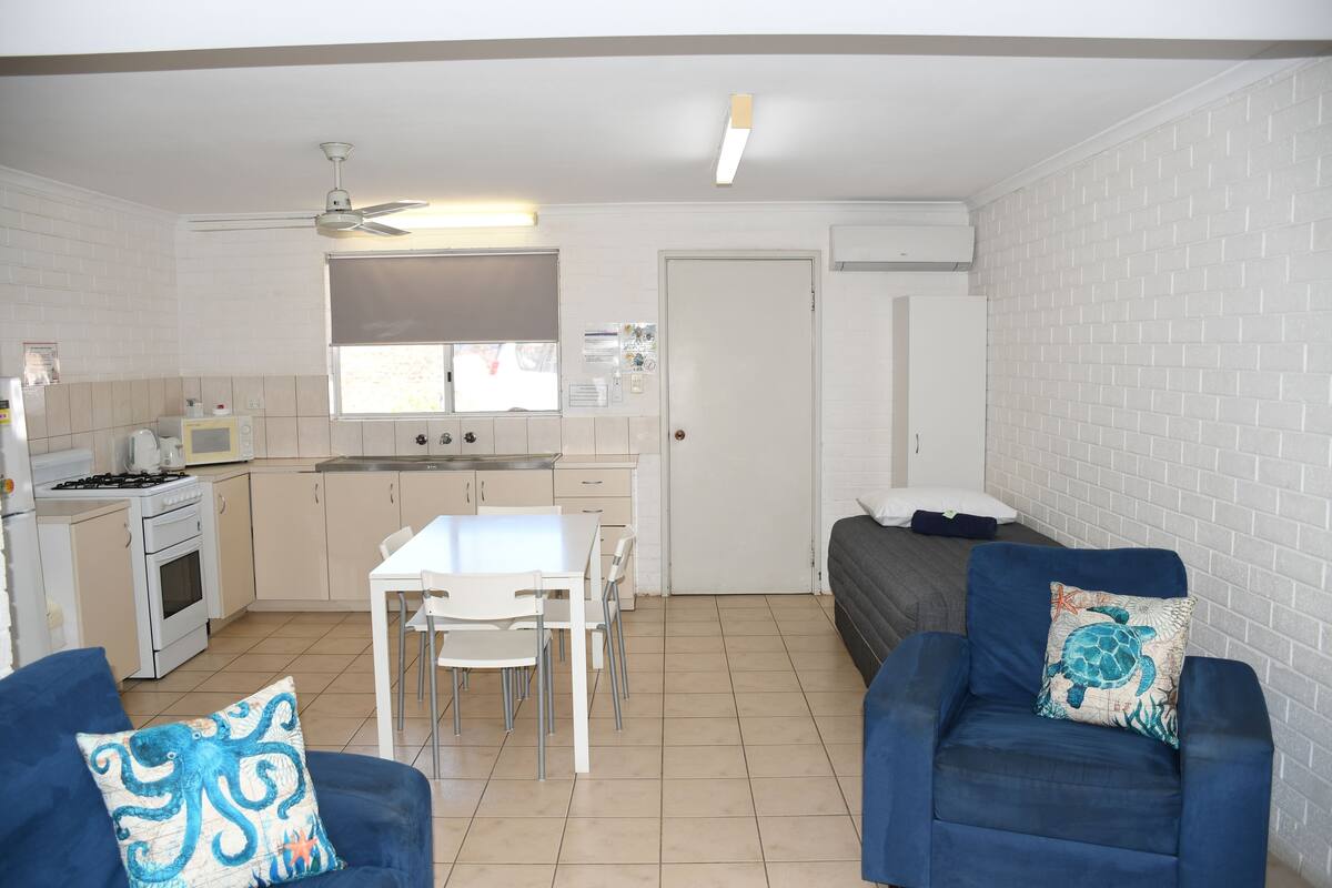Un espacio habitable compacto con kitchenette, zona de comedor y área de estar con sofá y sillas.