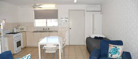 Un espacio habitable compacto con kitchenette, zona de comedor y área de estar con sofá y sillas.