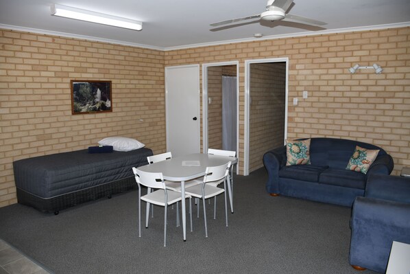 A room with a bed, a table with chairs, a sofa, and a ceiling fan.