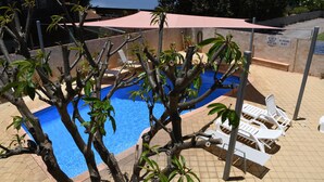 Ein Schwimmbecken mit gefliestem Sonnendeck, umgeben von Liegestühlen und einem überdachten Bereich.