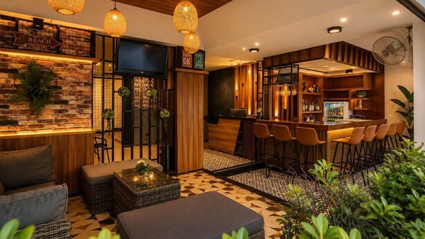 A modern bar area with a wooden bar counter, multiple stools, and a television screen. - The Mantra Hotel (Karon)