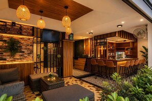 A modern bar area with a wooden bar counter, multiple stools, and a television screen. - The Mantra Hotel (Karon)