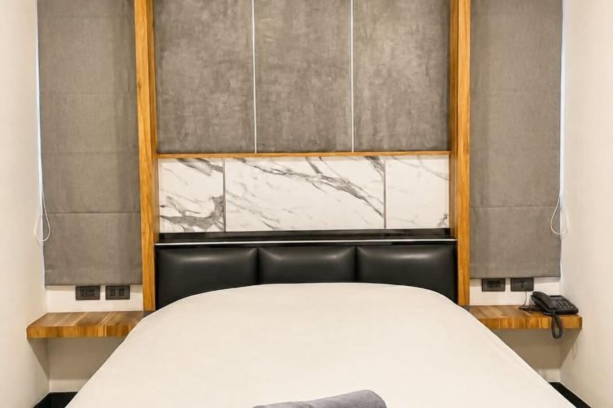 A bedroom with a bed, a headboard with a marble pattern, a wooden frame, and a telephone on a wooden shelf.