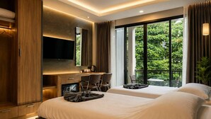A modern hotel room with a large bed, a desk with a chair, a TV, and a balcony with a view of greenery. - The Mantra Hotel (Karon)