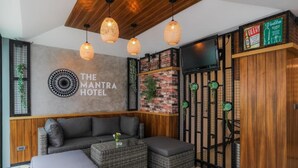A modern hotel lobby with a sofa, ottomans, a wall-mounted TV, and a sign for 'The Mantra Hotel'. - The Mantra Hotel (Karon)