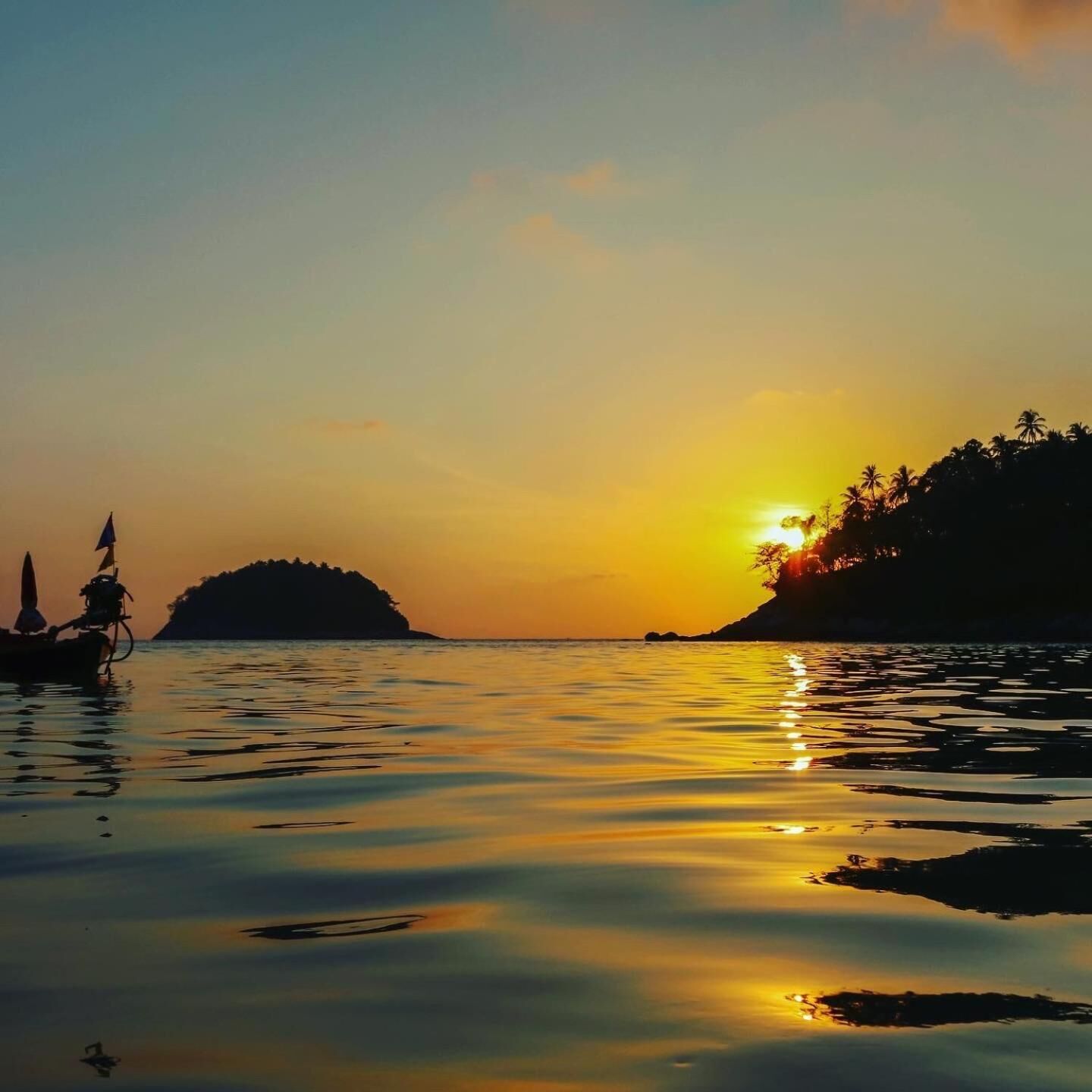 A calm body of water with a boat on the left and a sunset in the background.