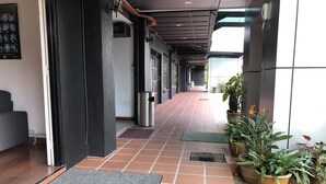 A corridor with tiled flooring, a metal trash bin, potted plants, and a grey mat at the entrance.
