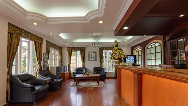 A reception area with a wooden reception desk, two leather armchairs, a coffee table, and a chandelier.