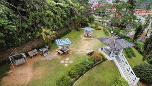 A lush garden with a gazebo, outdoor seating, and a staircase leading to a building.