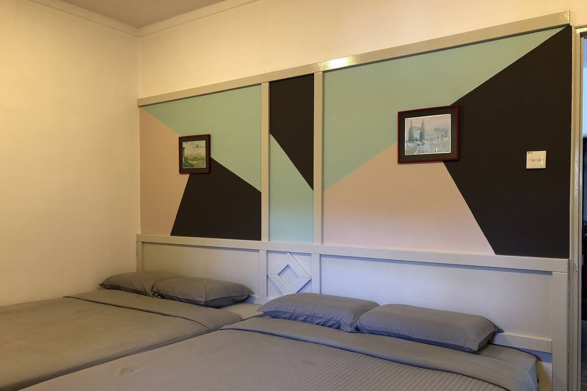 A room with two single beds, each with a pillow and a blanket. There are two framed pictures on the wall above the beds.