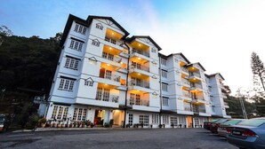 A multi-story hotel with balconies, a parking lot, and a mountainous backdrop.
