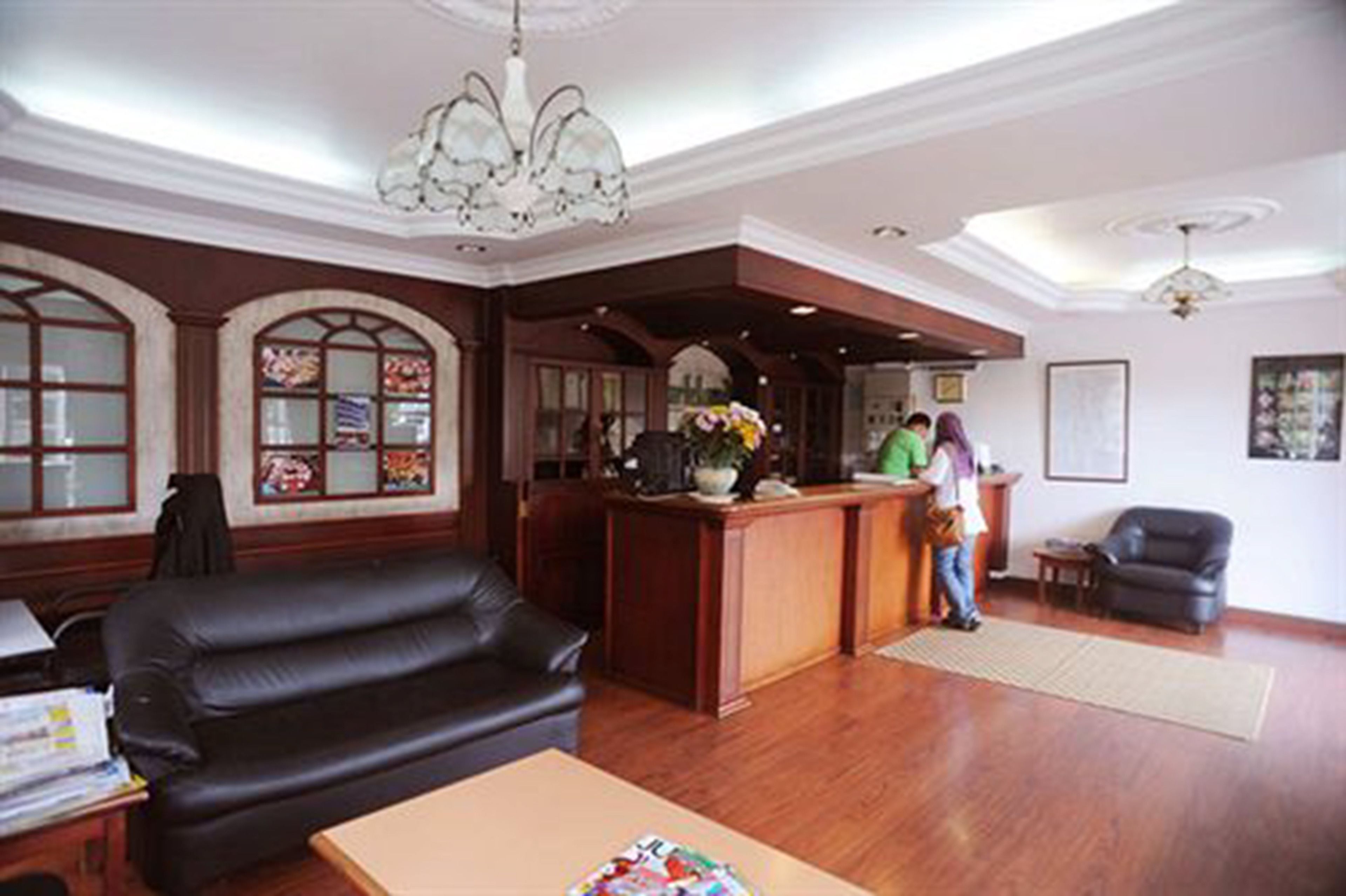 A lobby with a reception desk, a black leather sofa, wooden flooring, and a chandelier.