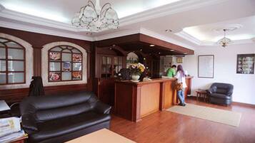 A lobby with a reception desk, a black leather sofa, wooden flooring, and a chandelier.