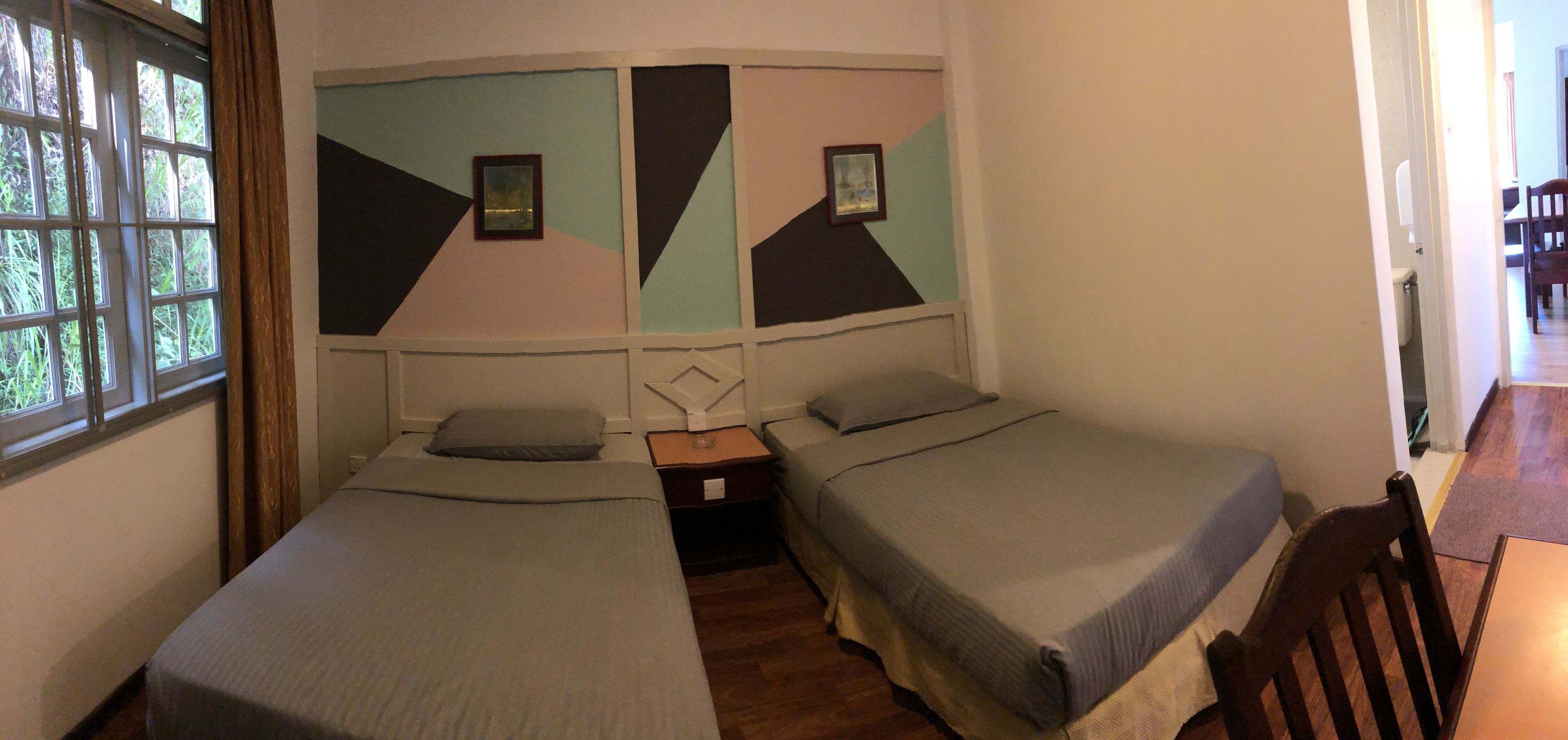 Ein Zimmer mit zwei Betten, einem Fenster und einer Tür zu einem anderen Raum.