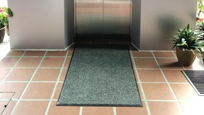 A modern elevator with a metallic finish, a control panel with an upward arrow, and a doormat at the entrance.