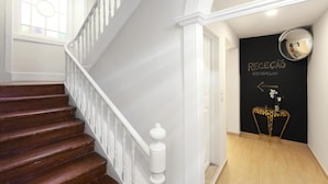 A staircase with a white railing leading to a reception area with a black wall and a gold-framed mirror. - Urban City (Aveiro)