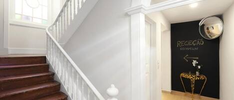 Una escalera con barandilla blanca lleva a una zona de recepción con pared negra y un espejo con marco dorado.