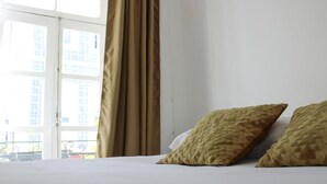 A hotel room with a bed, two pillows, a window with curtains, and a view of buildings outside. - Urban City (Aveiro)
