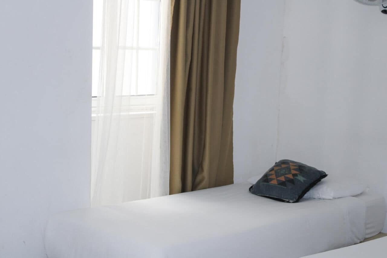 A room with a bed, a window with sheer curtains, and a brown curtain.