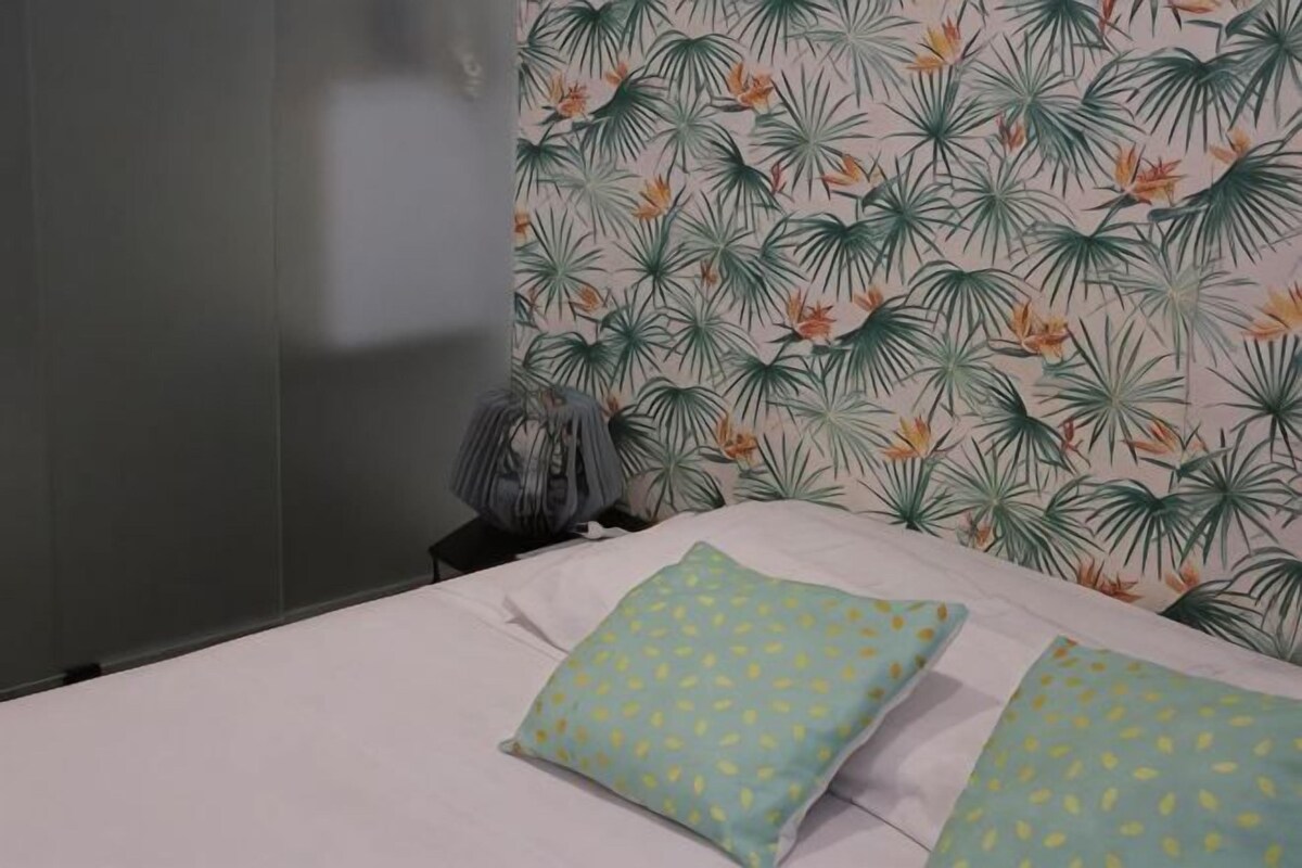 A bedroom with a bed, pillows, a nightstand, and a wall with a tropical leaf pattern.