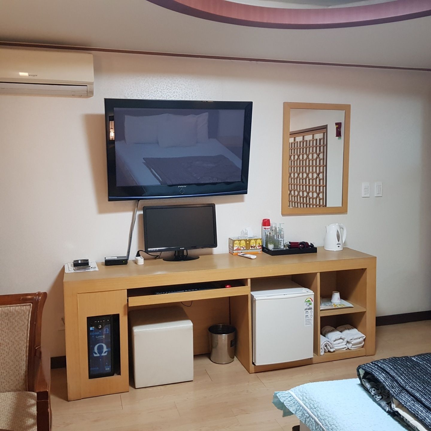 A hotel room with a TV, a small fridge, a mini-fridge, a desk with a computer, and a bed with a blanket.