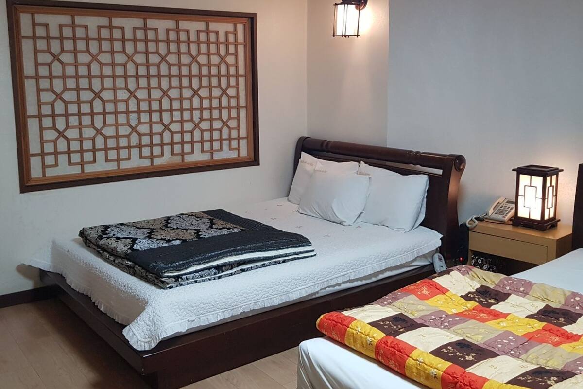 Un dormitorio con cama, mesita de noche, lámpara de pared y un separador decorativo.