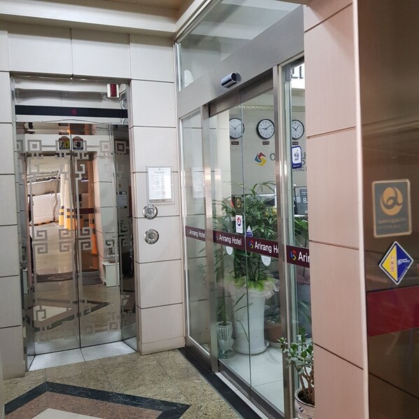 Entrada de un hotel con puerta de vidrio, un reloj y un letrero que indica el Hotel Arirang.