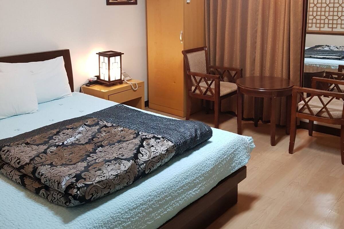 Una habitación de hotel con cama, escritorio, silla, armario y una pequeña mesa.