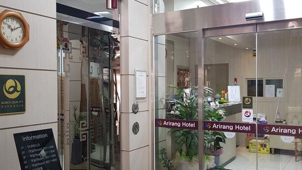 Zona reception di un hotel con una porta in vetro, una sveglia e un cartello che indica l'Hotel Arirang.