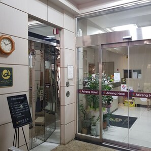 A hotel reception area with a glass door, a clock, and a sign indicating the Arirang Hotel.