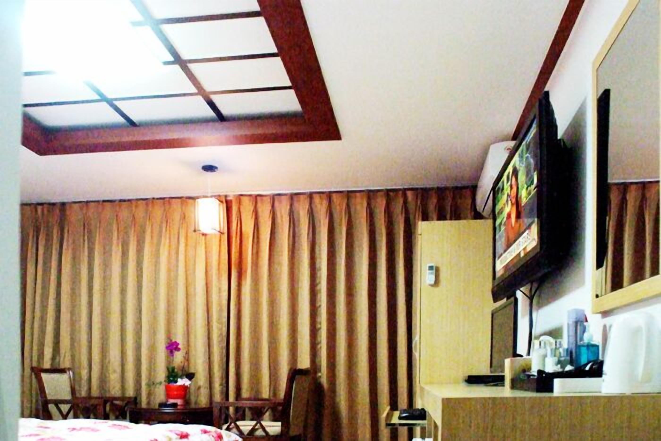 Habitación de hotel con cama, escritorio, silla, televisor y ventana con cortinas.