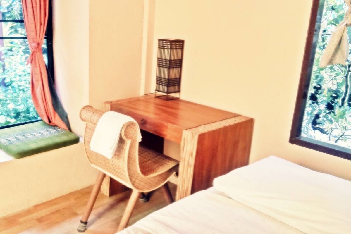 A room with a wooden desk, a chair, a bed, and a window with curtains.