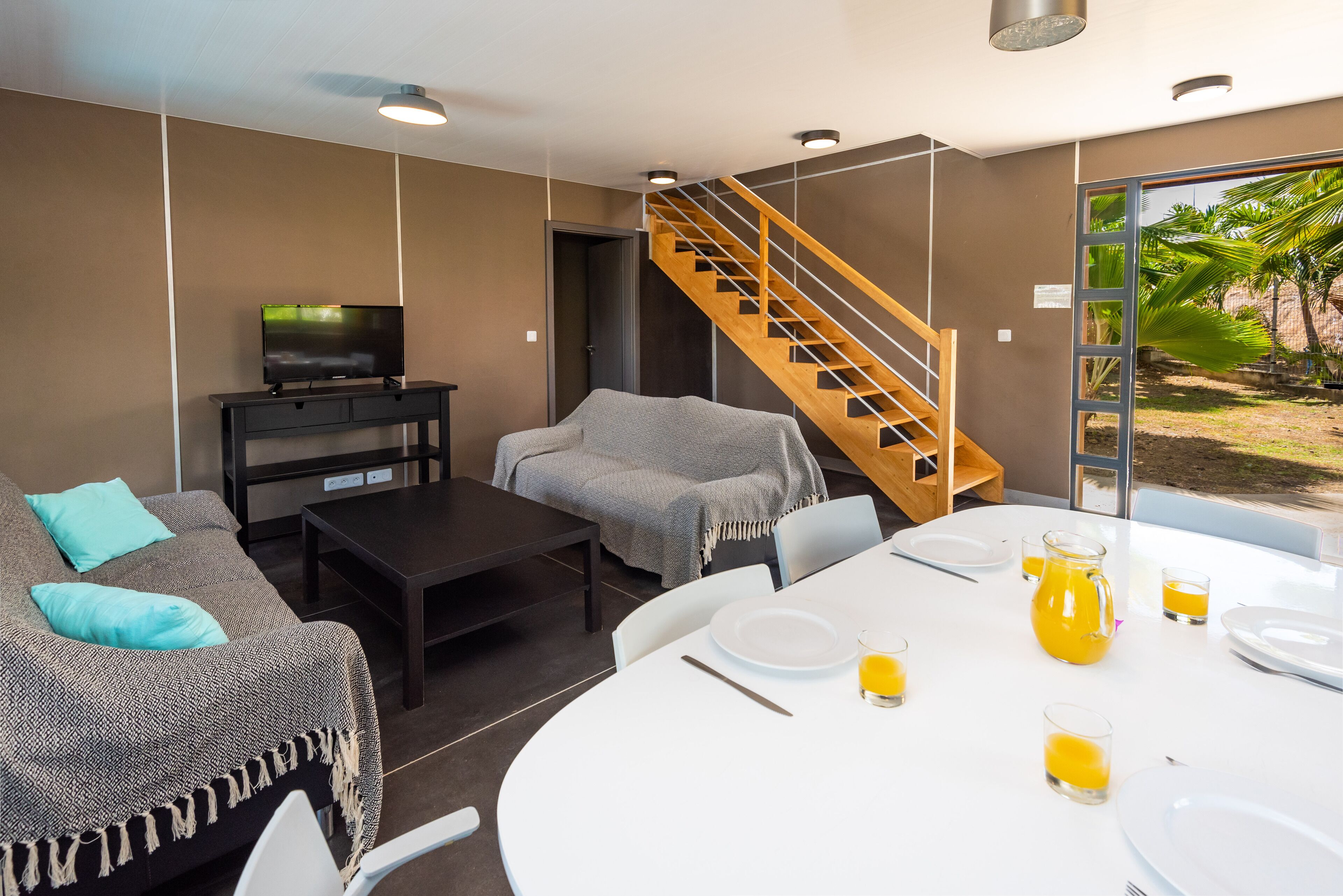 A modern living room with a sofa, TV, and dining area with a table set for two.