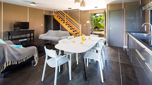 A modern kitchen with a built-in oven, a dining area with a white table and chairs, and a staircase leading to a balcony.