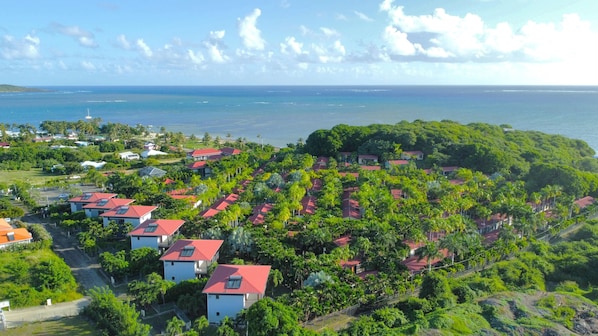 An aerial view of a coastal resort with multiple buildings, lush greenery, and a view of the ocean. - Le Village de la Pointe (Le Vauclin)